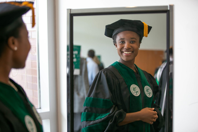 Student admires self in mirror, wearing regalia.